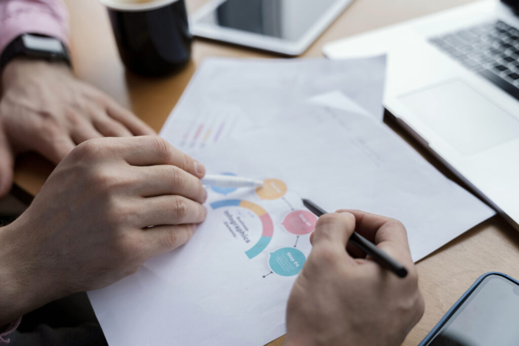 Paper with graphics and hands with pencils pointing to it